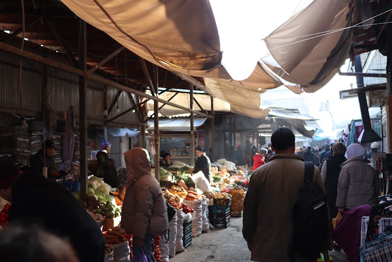 Vendors and shoppers moving through a covered outdoor bazaar with produce stalls in winter light