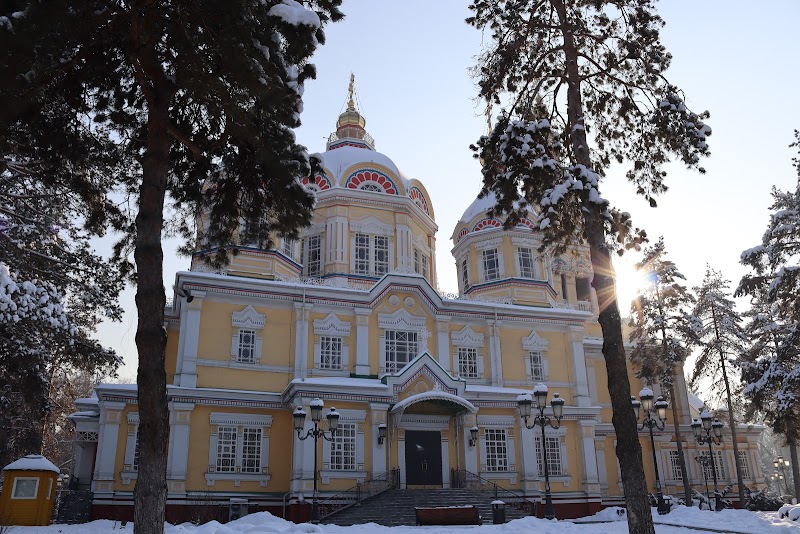 Yellow and white Ascension Cathedral in Almaty surrounded by snow-covered trees and morning sunlight