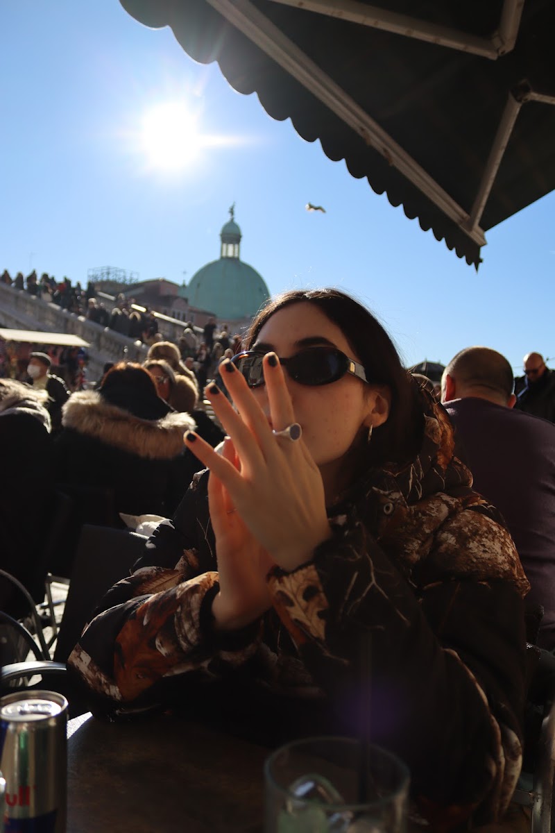 Woman at a sunlit outdoor café table with a green dome and blue sky over Venice behind her