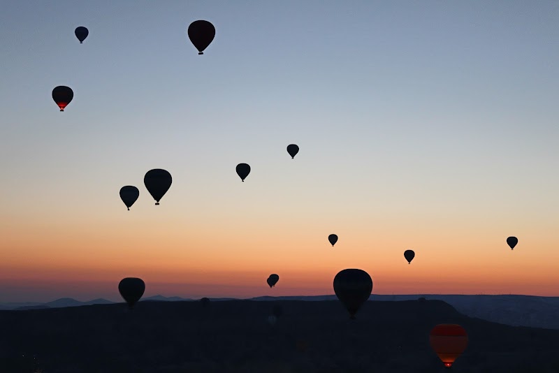 Silhouettes of hot air balloons drifting across an orange and blue sunrise sky over Cappadocia