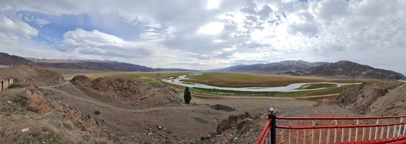 Panoramic view of the Naryn River winding through a broad arid valley with snow-capped mountains on the horizon