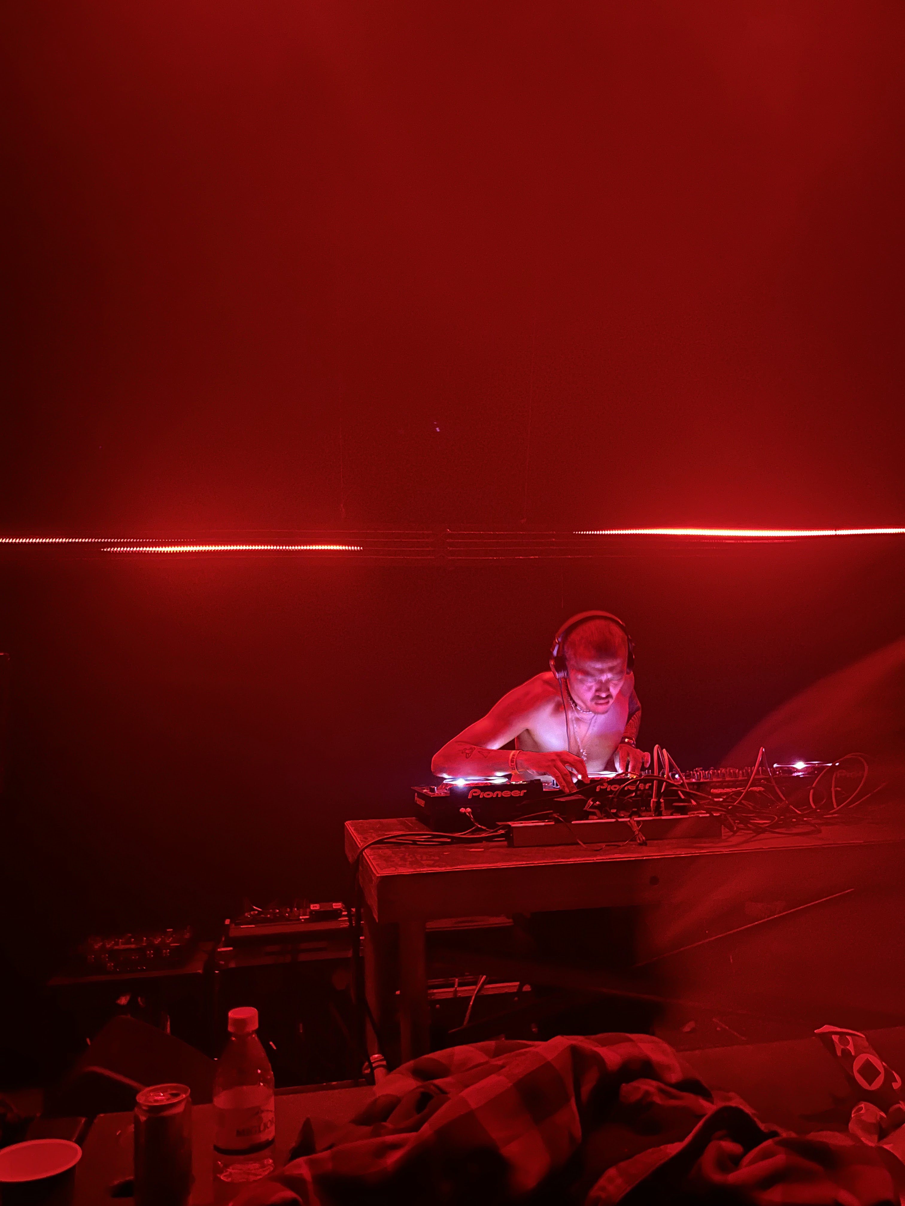 DJ hunched over Pioneer decks bathed entirely in red stage light in a dark club