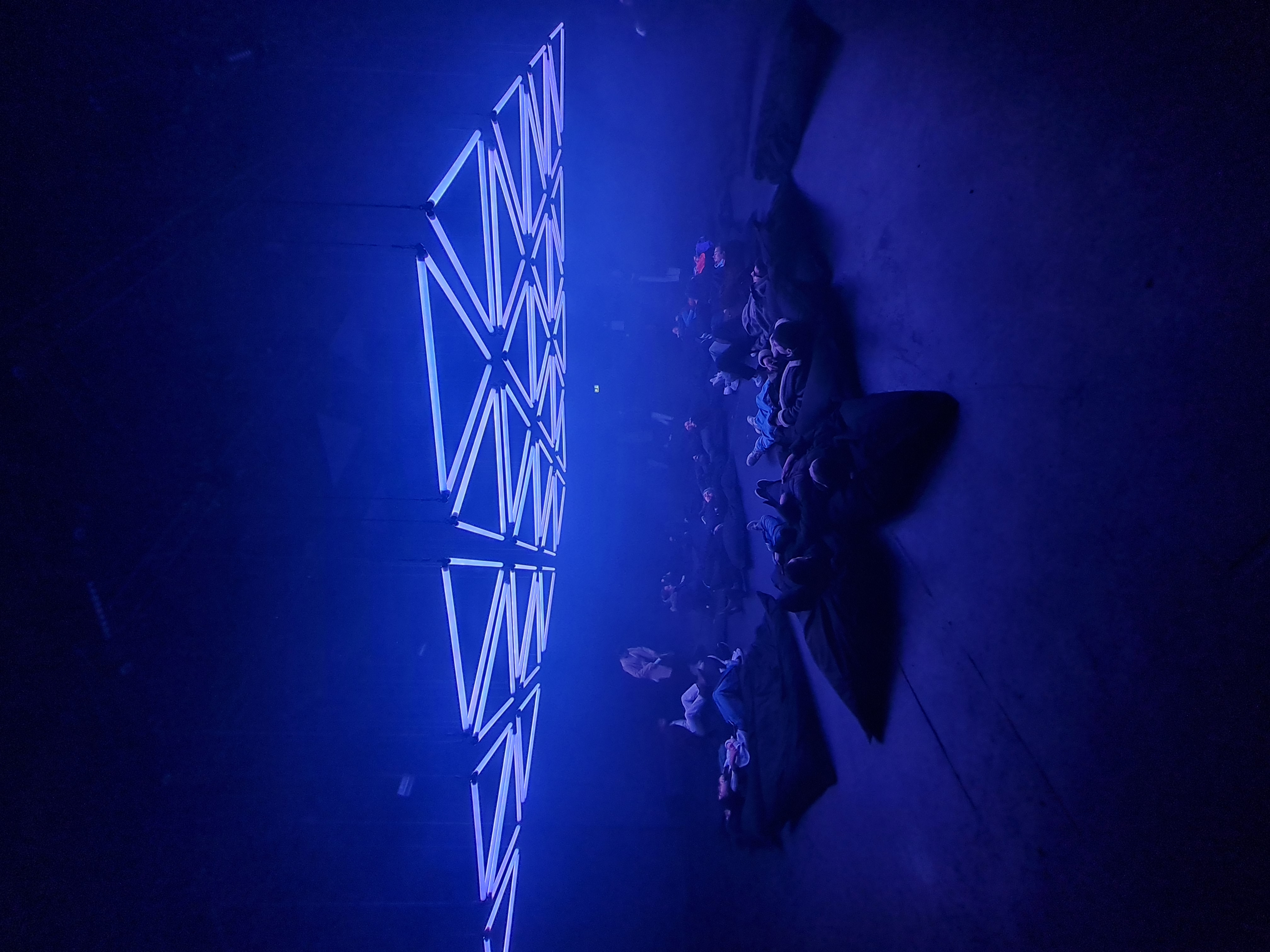 Glowing white geometric neon light installation flooding a dark club in blue light with crowd silhouettes