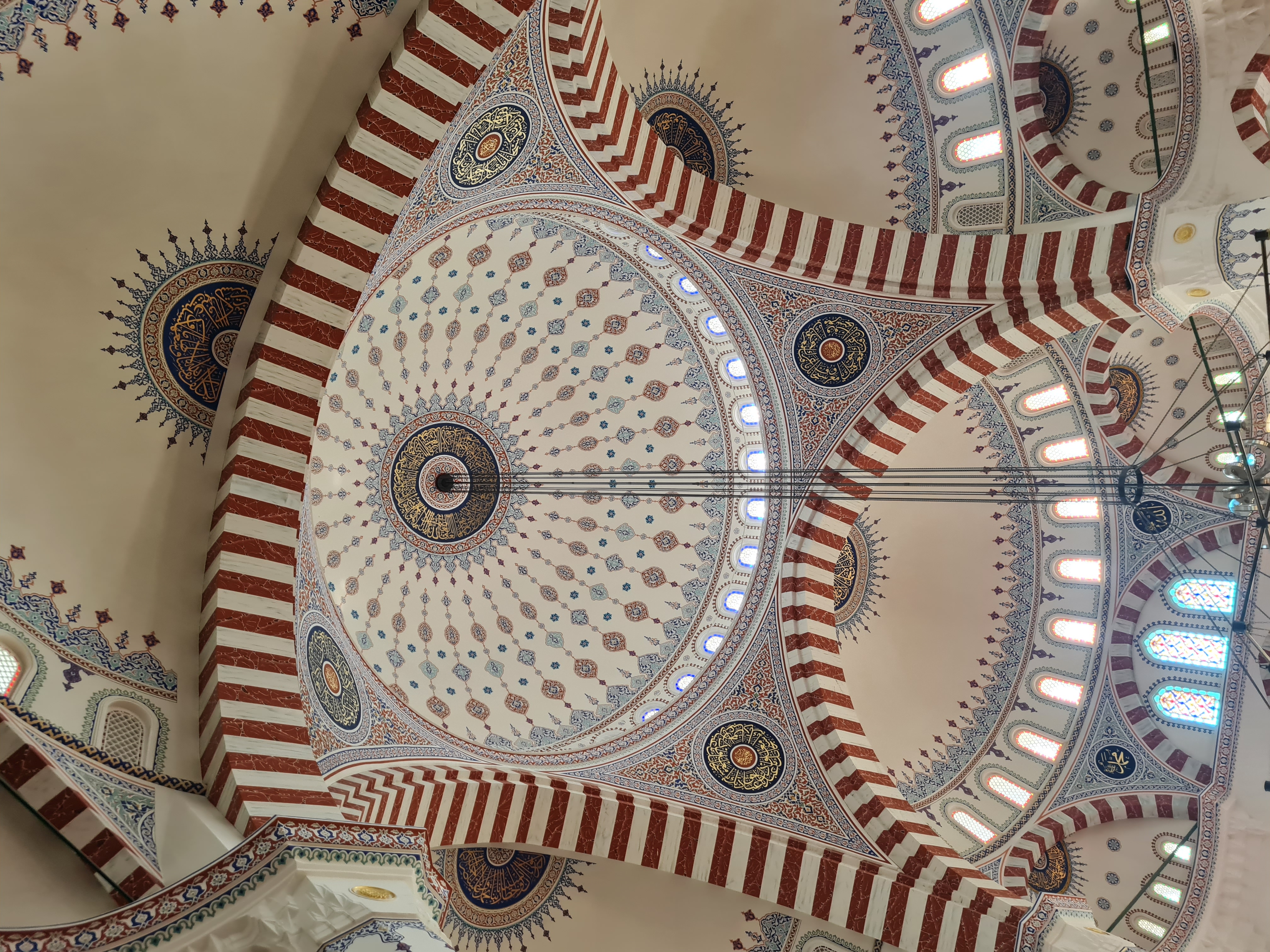 Looking straight up at the intricate red-and-cream striped arches and central dome of the Ertugrul Gazi Mosque