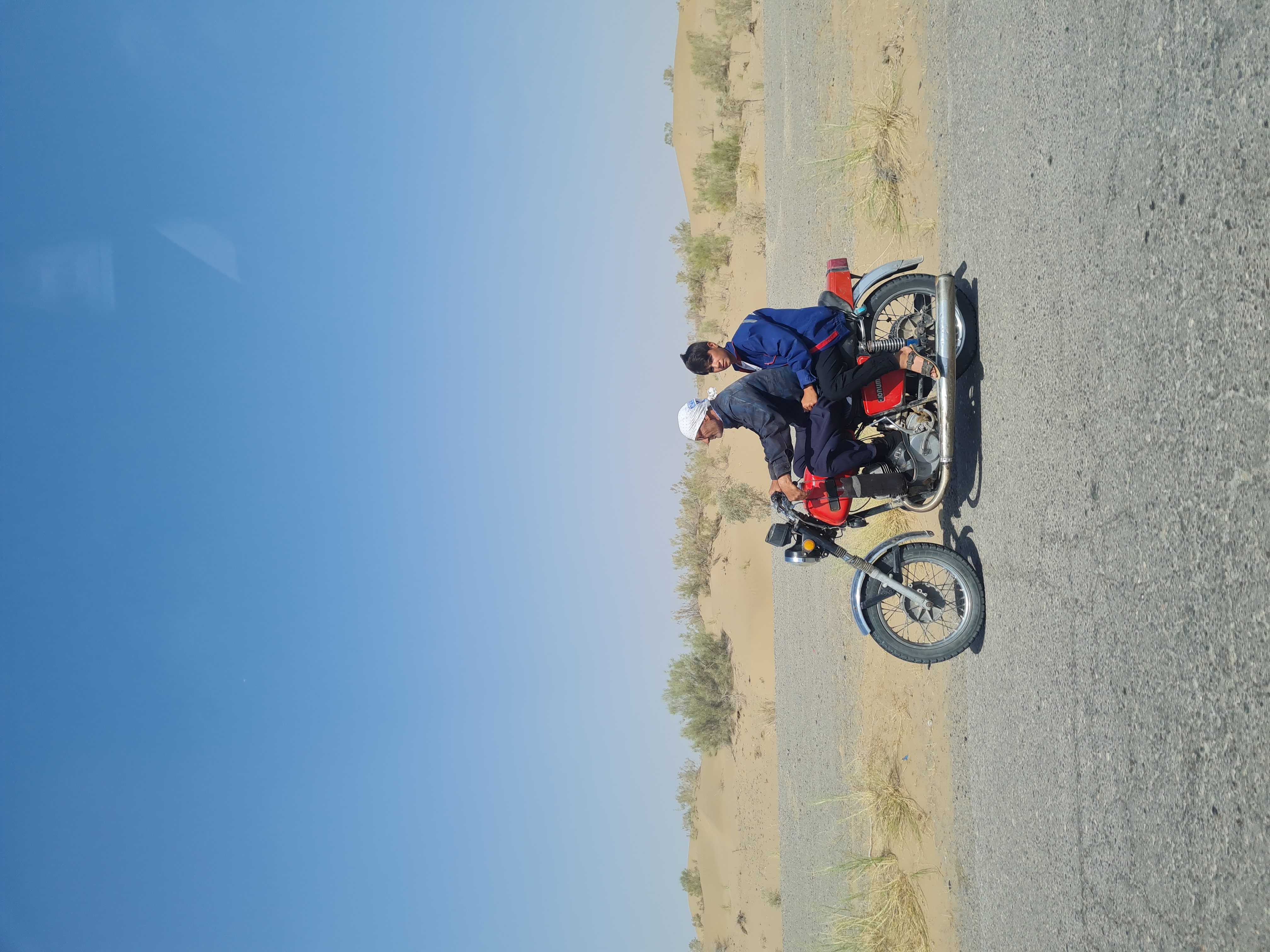 Two riders sharing a motorcycle on a dusty desert road through the Turkmen steppe
